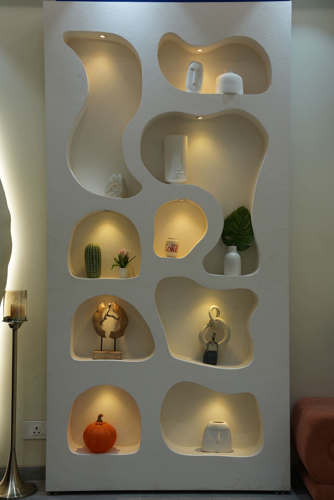 The aesthetic wall set: a freestanding cabinet of individually lit, organically shaped niches holding styled objects.