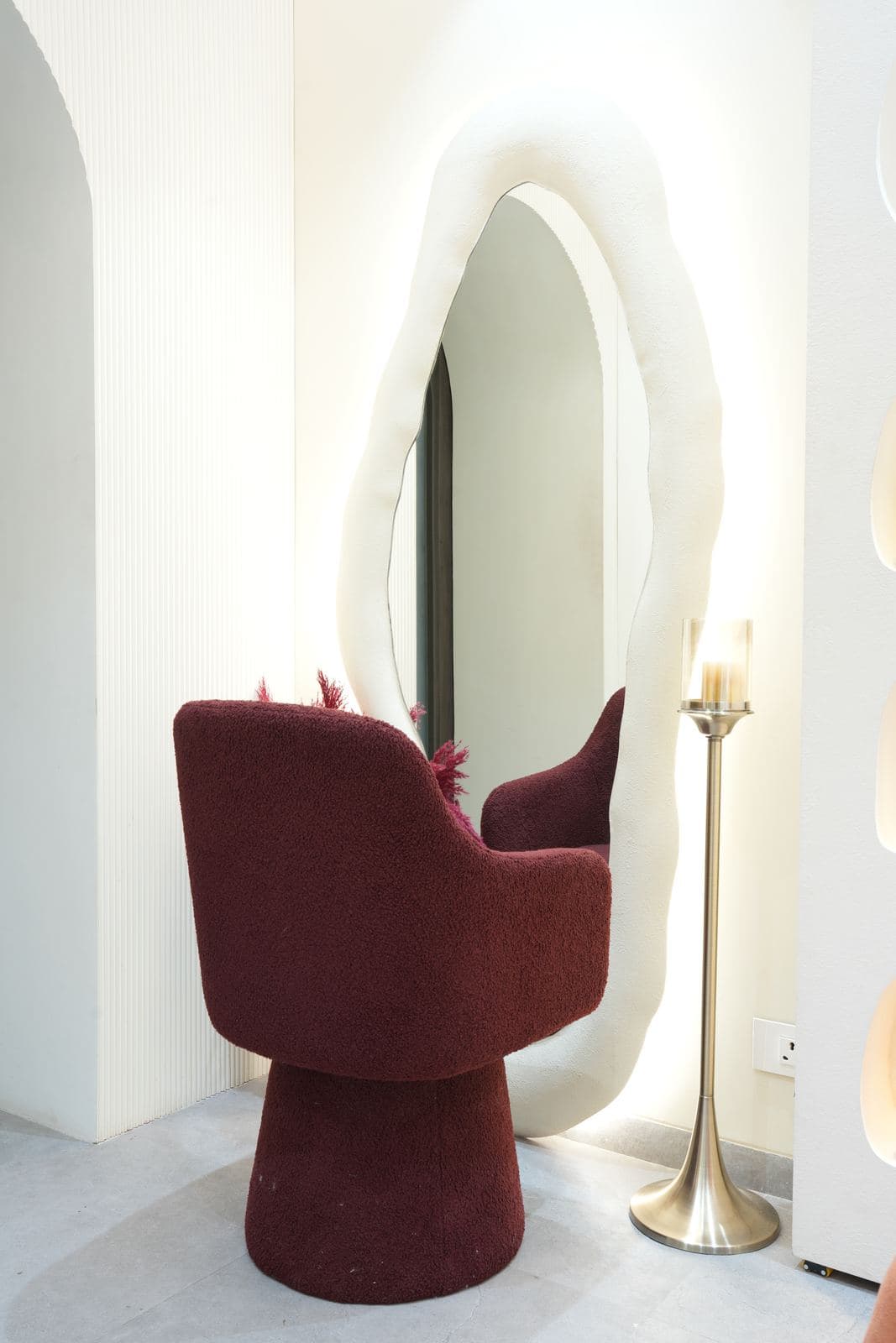 The dressing and makeup set: a burgundy bucket chair in front of a backlit organic-shaped mirror.