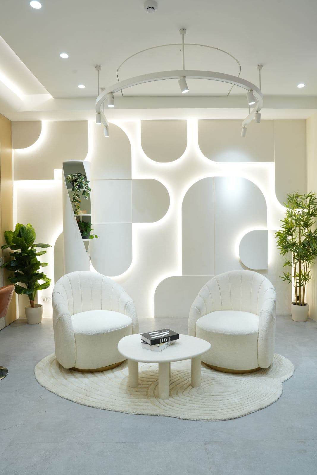 The podcast set: two cream bucket chairs and a round table in front of the illuminated sculptural niche wall, under the studio's ceiling lighting rig.
